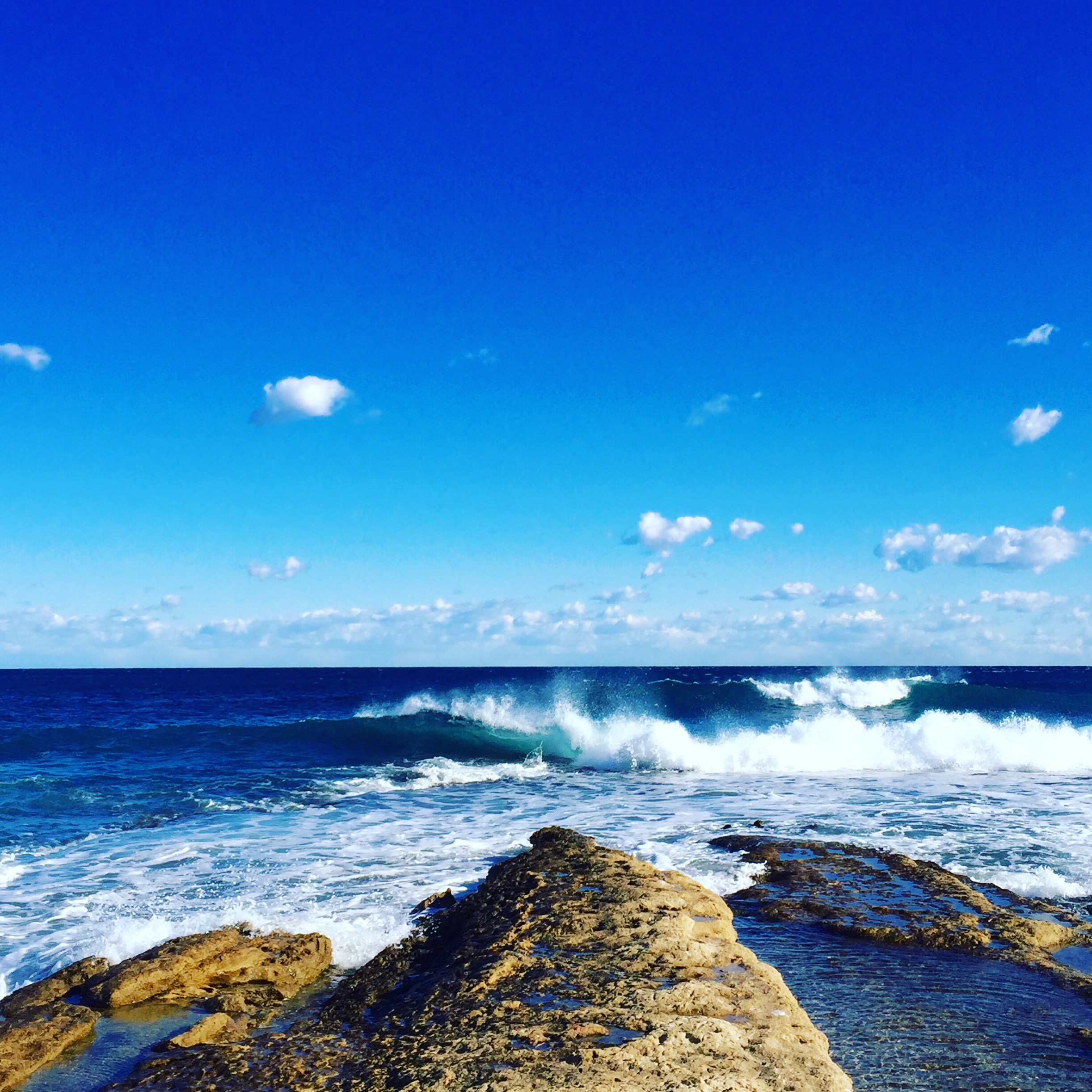 Paisaje de mar, cielo azul, con olas rompiendo en las rocas